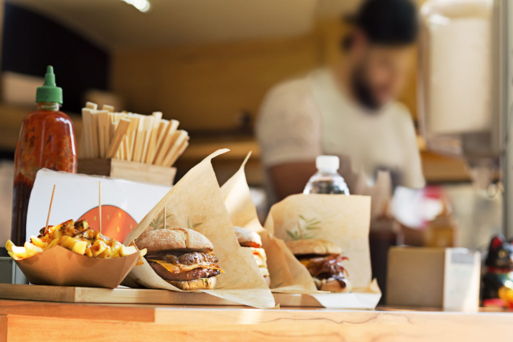 burgers and fries sitting on a food truck counter. Chef is visible in background preparing other food.