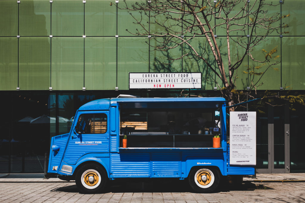 photo of a blue vintage food truck parked in front of urban building on a city street