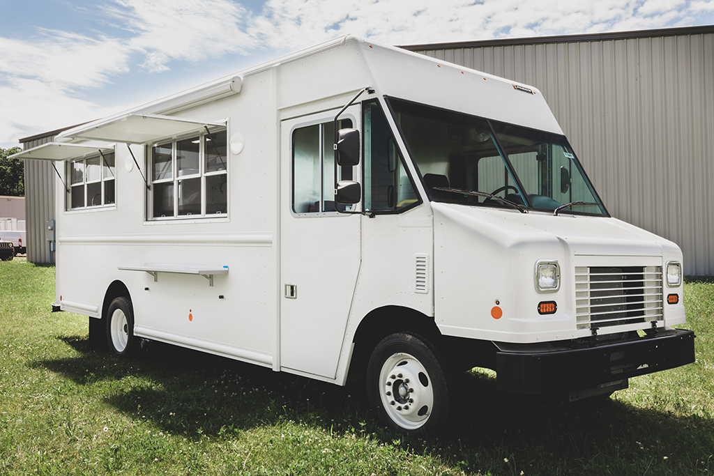 photo of a white food truck parked in grass in front of a warehouse